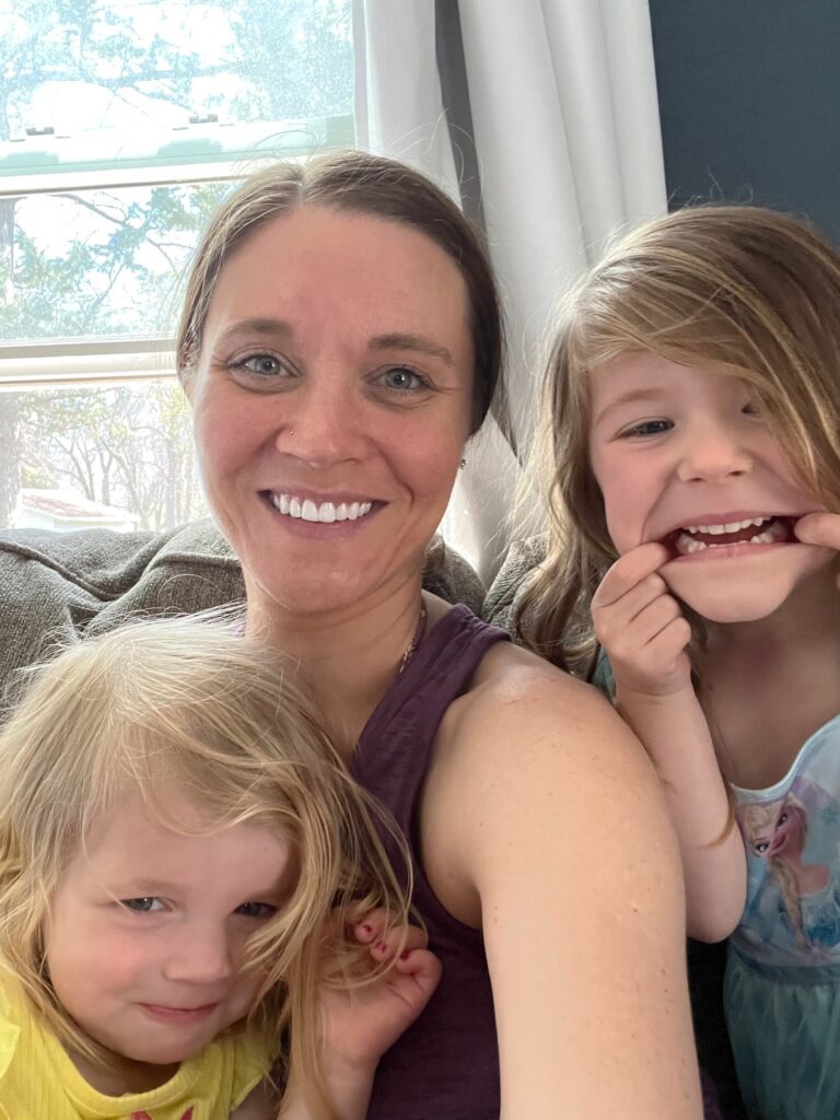 Everyday with Faith blogger smiling with her two young daughters in a bright living room.