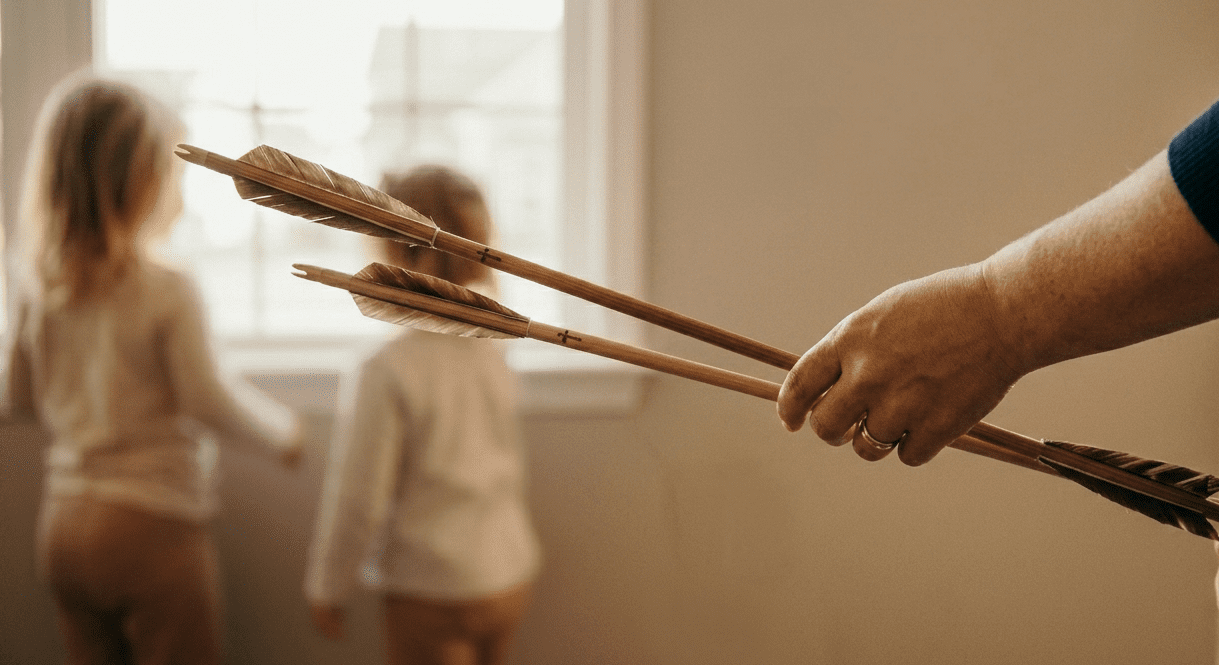 Two wooden arrows held by a mother with toddlers in the background, representing Psalm 127:4 and meaningful Christian graduation gifts