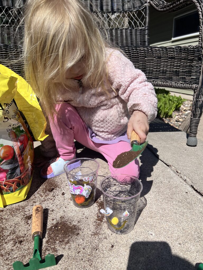 Scooping soil outside for a messy grass in a cup activity for toddlers.